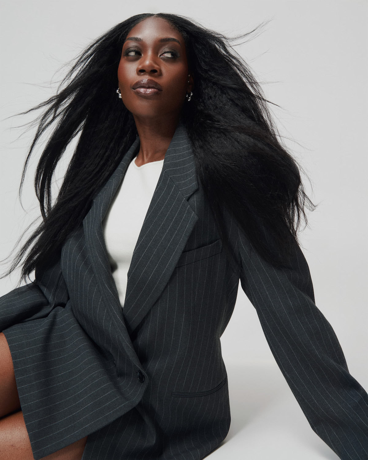 Woman wearing a black pinstripe blazer over a white top on a light gray background